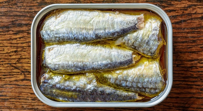 An open can of sardines in oil on a weathered wooden table seen from above.